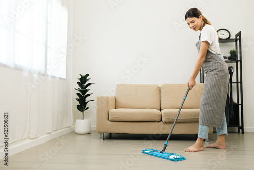 Young beautiful woman with apron and rubber glove with mop ready for cleaning home. Housekeeping housework or maid worker holding mop cleaning floor