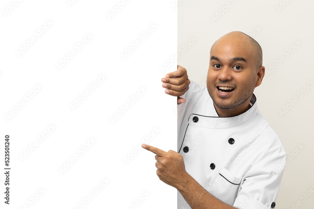 Happy Young handsome asian man chef in uniform looks out from behind an empty whiteboard. Cooking indian man hiding behind big blank billboard for advertising text menu in kitchen and restaurant. Happy Young handsome asian man chef in uniform looks out from behind an empty whiteboard. Cooking indian man hiding behind big blank billboard for advertising text menu in kitchen and restaurant.
