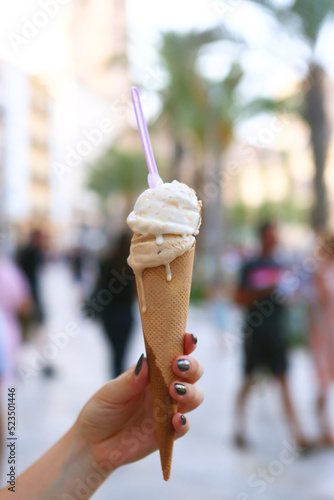 melting ice cream cone in human hand close up photo on city center background