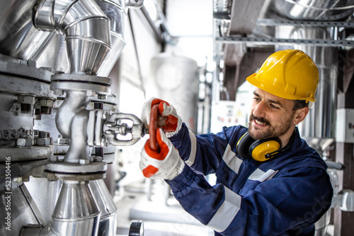 Refinery factory worker closing valve on gas pipeline in petrochemical industrial plant.