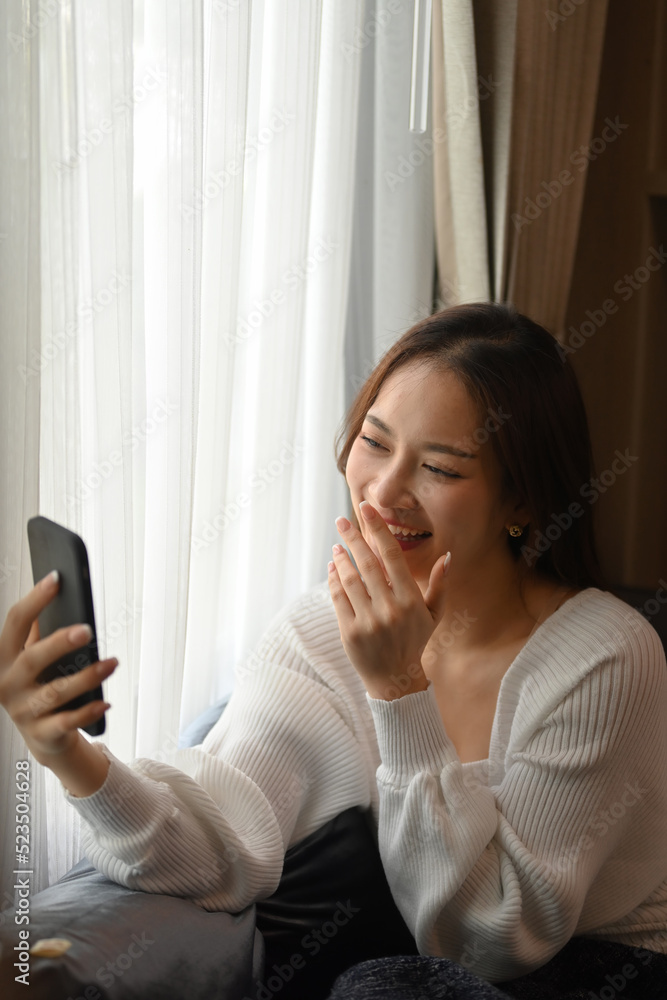 Cheerful young woman in warm warm sweater chatting online or making video call on her smart phone Cheerful young woman in warm warm sweater chatting online or making video call on her smart phone