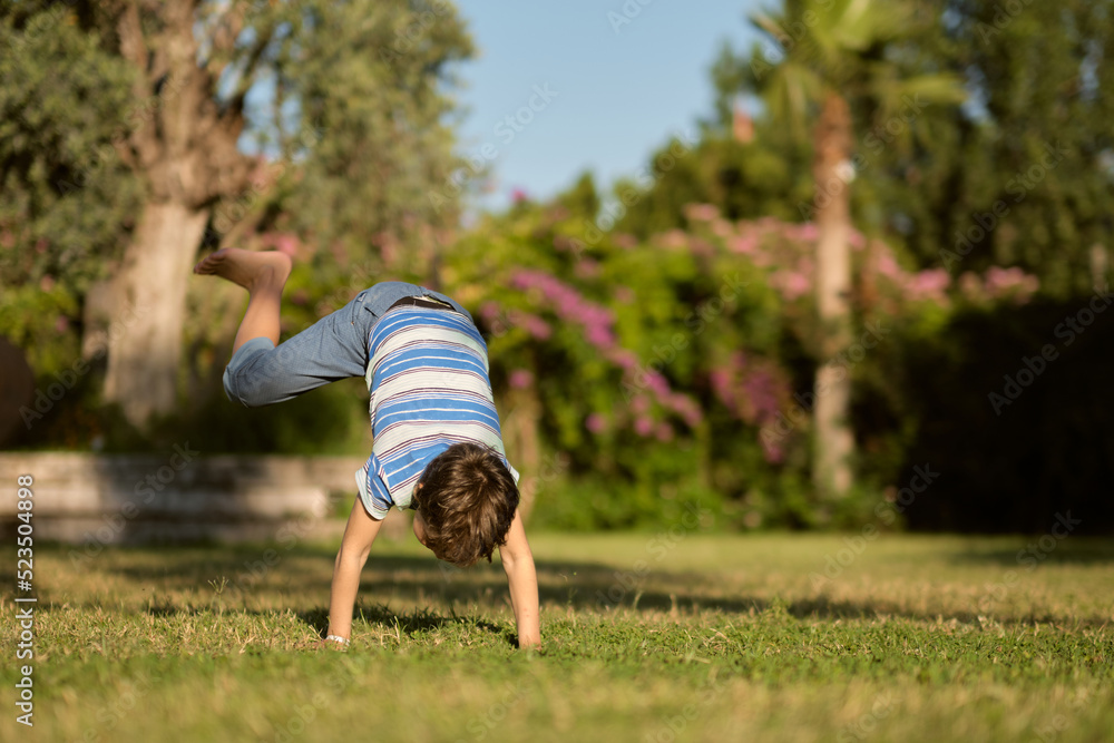 boy preschooler somersaults on the grass on a hot summer day.