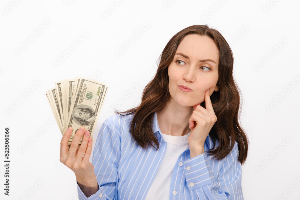 thoughtful brunette woman in blue shirt looks at dollars in her hands on white background thoughtful brunette woman in blue shirt looks at dollars in her hands on white background