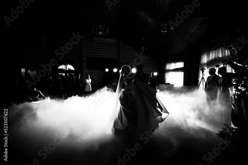Black and white photo of the first dance of newlyweds with lighting effects and confetti, silhouettes