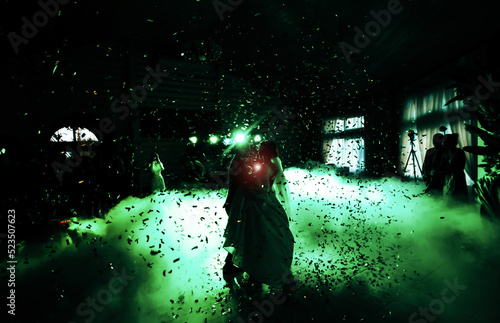 Black and green photo of the first dance of newlyweds with lighting effects and confetti, silhouettes