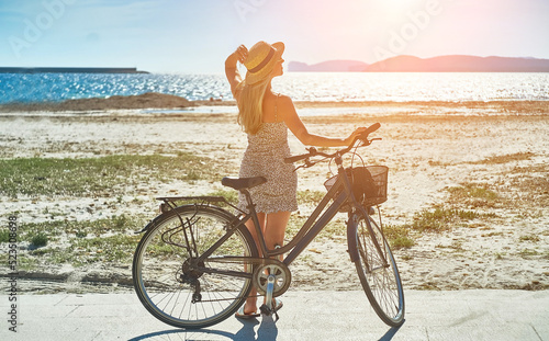 Carefree woman with bike riding on sand beach having fun, on the seaside promenade on a summer day.	
