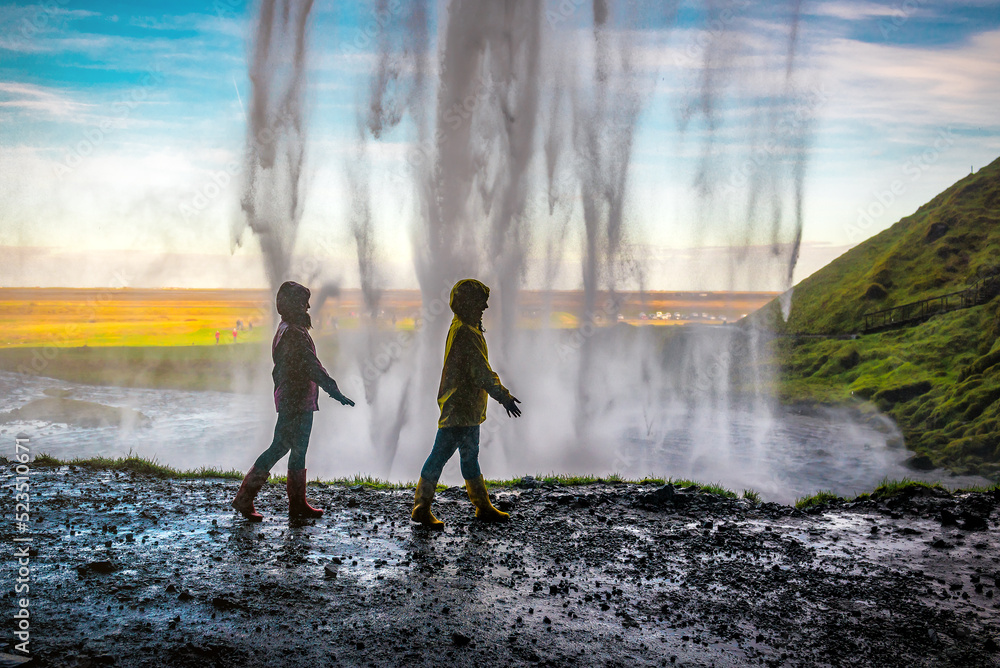 Obraz premium Two women walking under a waterfall Seljalandsfoss in Iceland