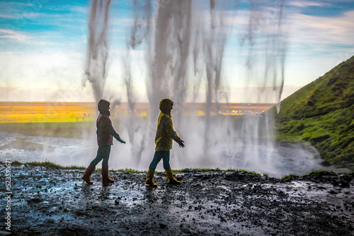 Two women walking under a waterfall Seljalandsfoss in Iceland