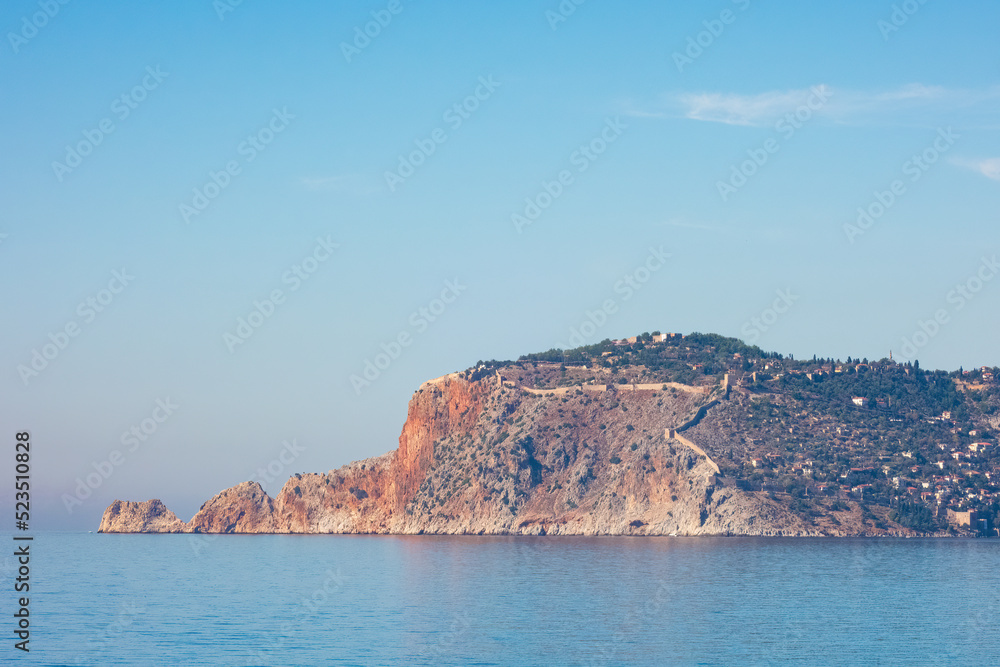 The Alanya Peninsula with old city fortress. View from the beach with calm sea