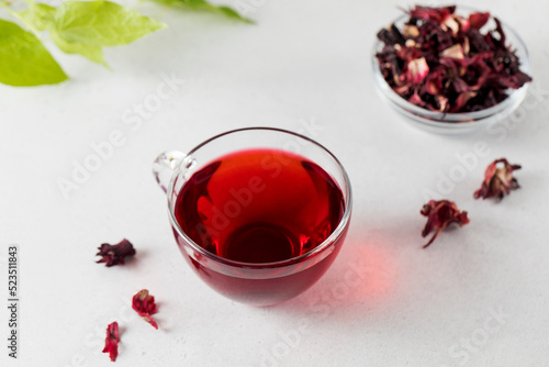 Herbal tea made from hibiscus petals in a transparent cup and a bowl of dry hibiscus.