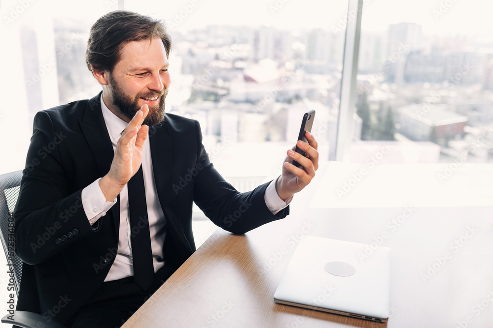 Business man having a video call on a smartphone. smiling guy doing video chat in the office. business man makes a welcoming gesture.