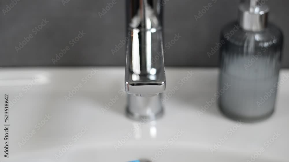 Blue toothbrush with toothpaste on it being held under water stream to make it wet for brushing teeth Blue toothbrush with toothpaste on it being held under water stream to make it wet for brushing teeth
