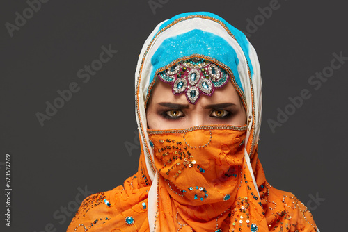 Studio shot of a chrming female wearing the colorful hijab decorated with sequins and jewelry. Arabic style. photo