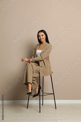 Beautiful young businesswoman sitting on stool near beige wall