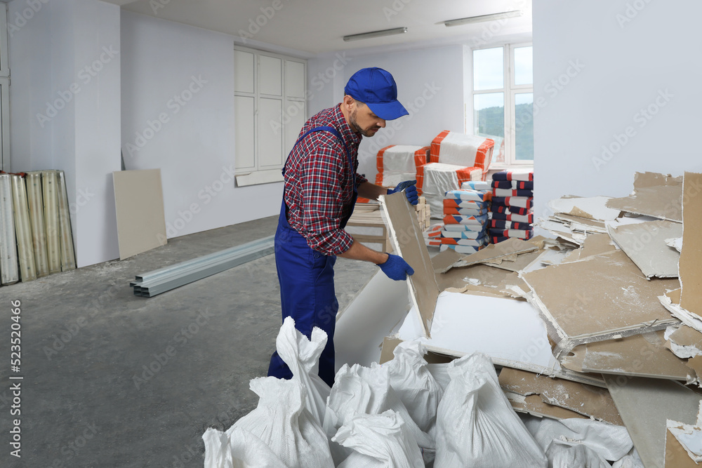 Construction worker carrying used drywall in room prepared for renovation Construction worker carrying used drywall in room prepared for renovation