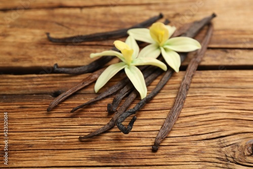 Aromatic vanilla sticks and flowers on wooden table, closeup