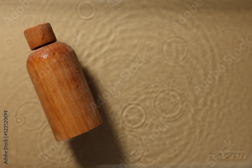 Wooden bottle of cosmetic product in water on beige background, top view. Space for text