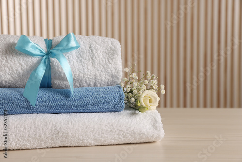 Soft towels, gypsophila and eustoma flowers on light wooden table, space for text