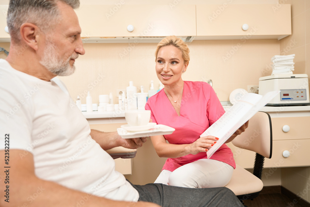 Cosmetologist woman shows price list to client and advises him Cosmetologist woman shows price list to client and advises him