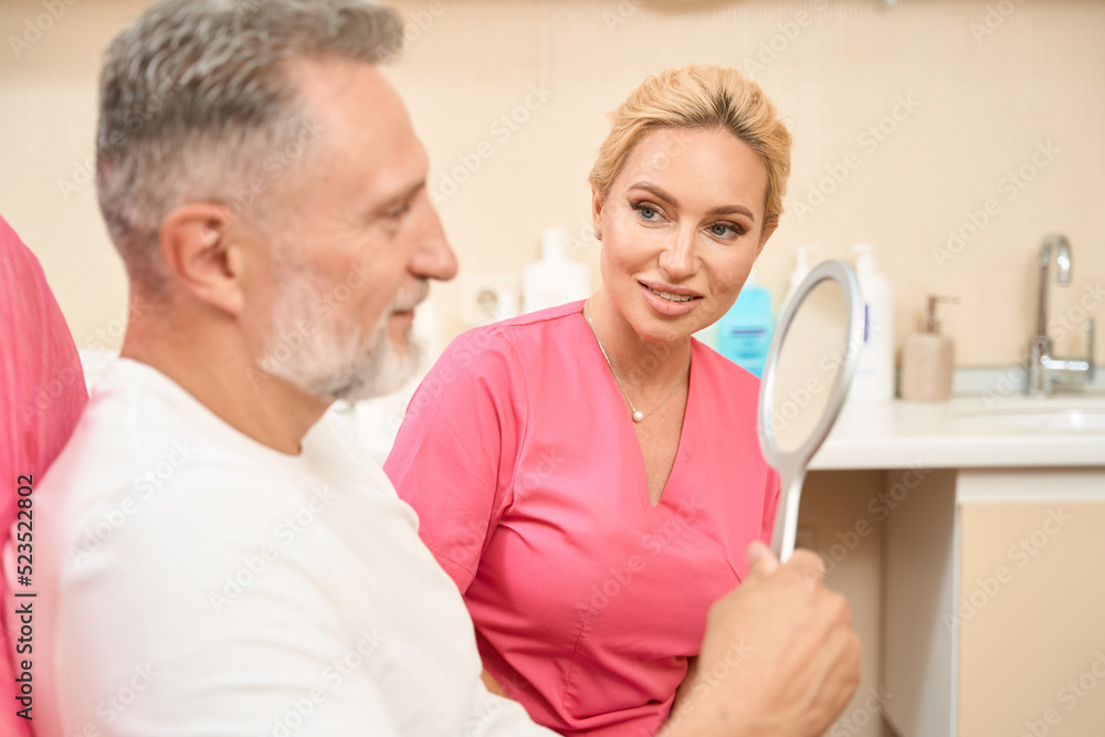 Adult man looks in mirror at consultation with woman beautician Adult man looks in mirror at consultation with woman beautician