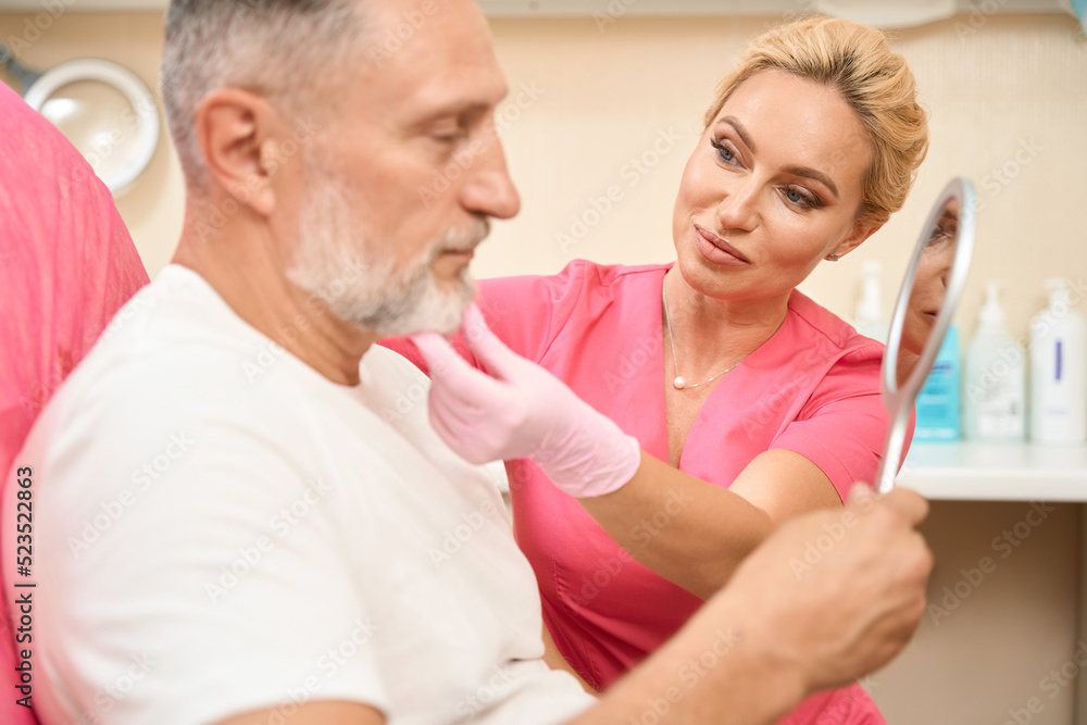 Obraz premium Man looks in mirror when woman beautician examines his face