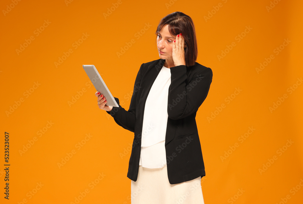 a businesswoman uses a tablet isolated on a yellow background with a calm thoughtful emotion. business online banking technology concept