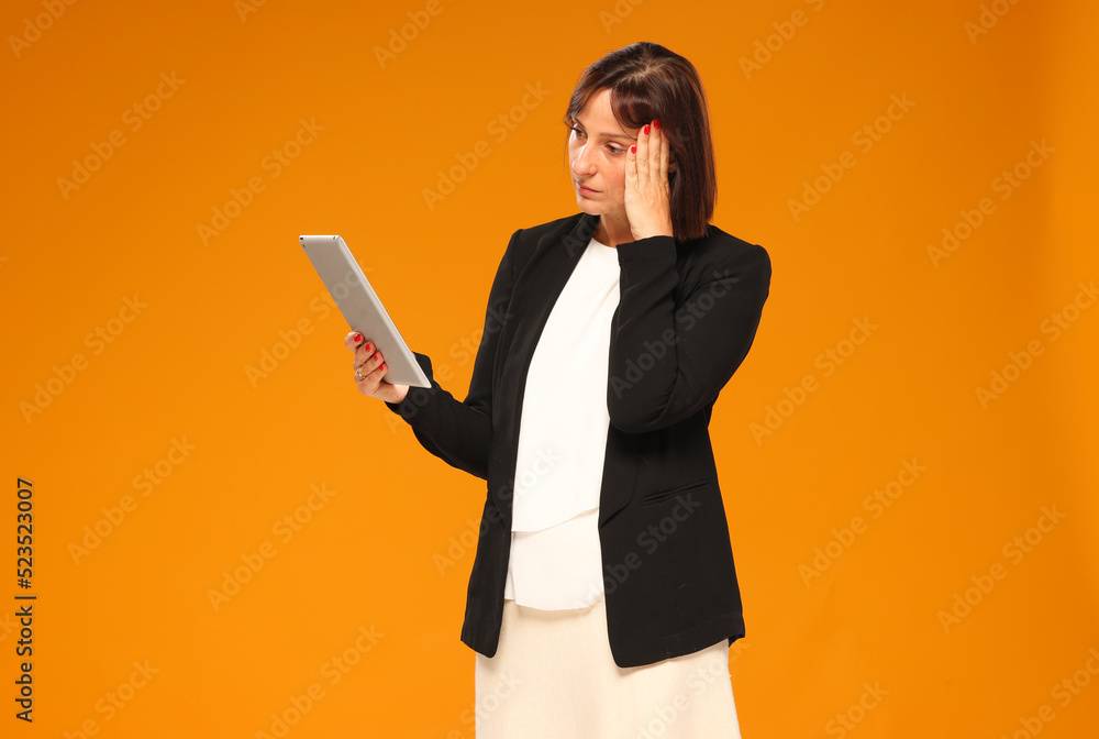 a businesswoman uses a tablet isolated on a yellow background with a calm thoughtful emotion. business online banking technology concept a businesswoman uses a tablet isolated on a yellow background with a calm thoughtful emotion. business online banking technology concept