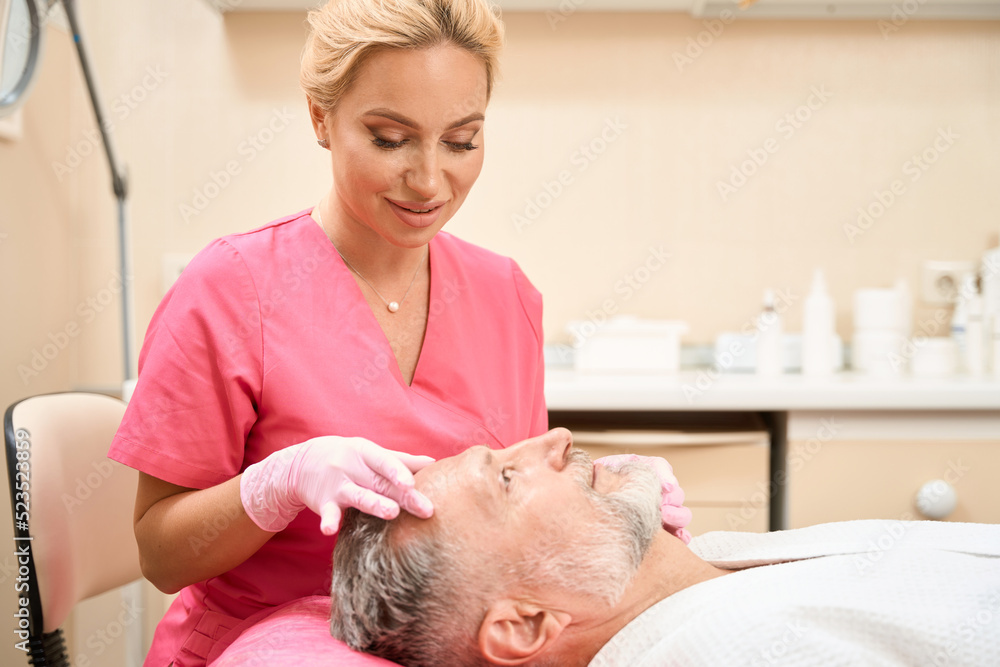 Fototapeta premium Smiling woman cosmetologist doing facial massage of man