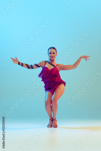 Canvas Print Portrait of young graceful flexible woman dancing ballroom dance without partner isolated on blue background in neon light