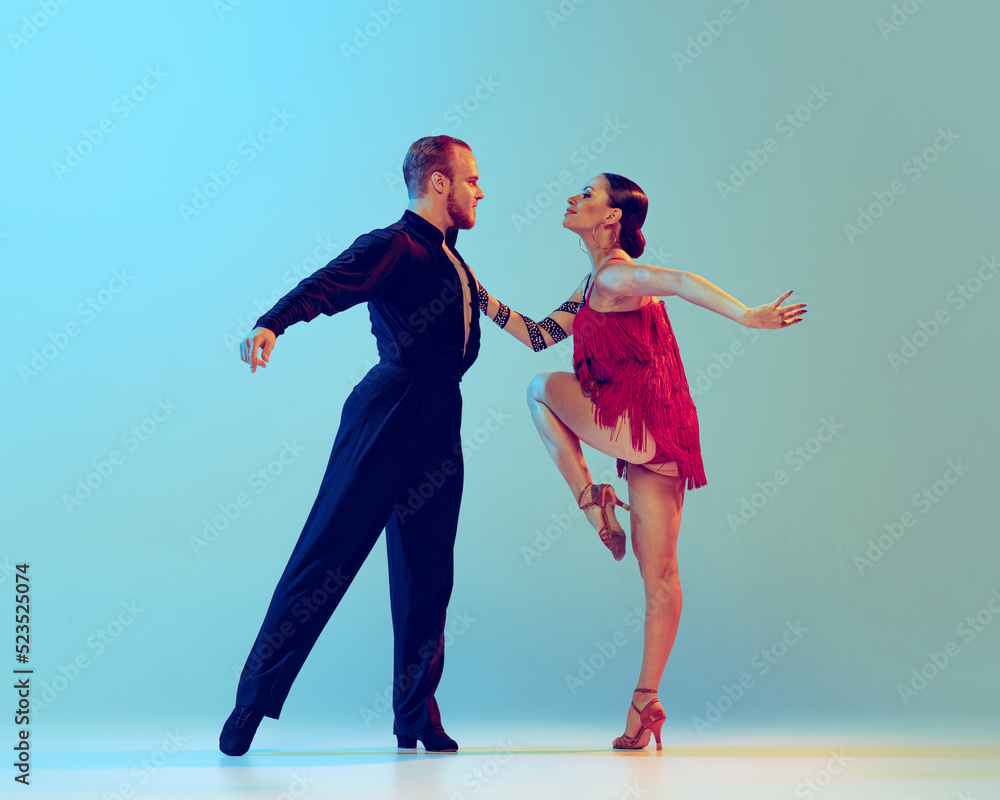 Naklejka premium Dynamic portrait of professional dancers in stage attires dancing ballroom dance isolated on blue background. Concept of art, beauty, music, style.