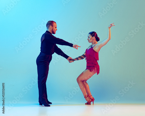 Beautiful woman and man, professional dancers dancing ballroom dance isolated on blue background. Concept of art, beauty, music, style.
