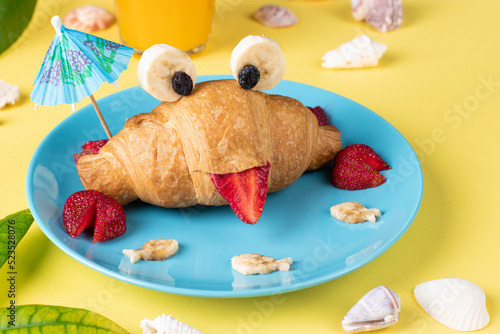 Fun food for kids - crab shaped croissant with strawberry and banana on yellow background