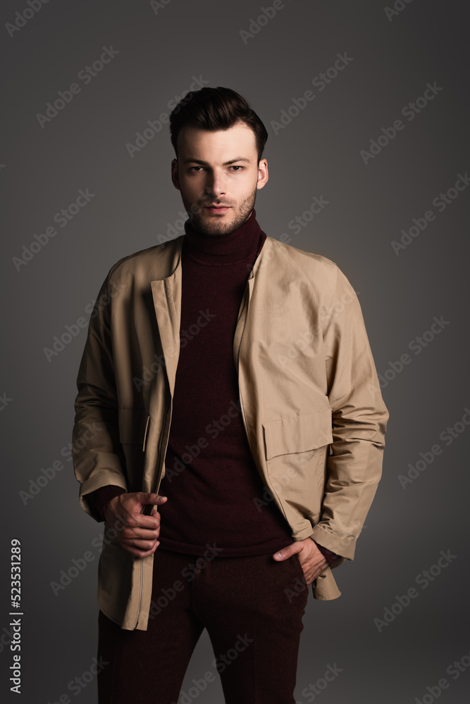 Stylish brunette man in jacket posing isolated on grey.
