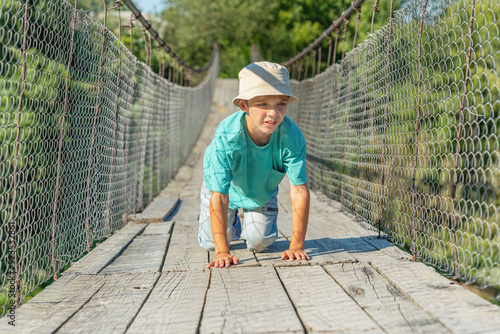 A boy who is afraid of heights crawls on all fours on a suspension bridge