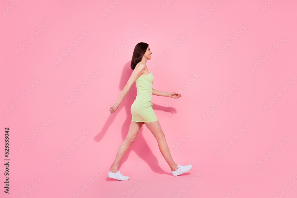 Full length photo of sweet shiny young lady wear green dress walking empty space isolated pink color background