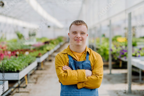 Young employee with Down syndrome working in garden centre, looking at camera with arms crossed.
