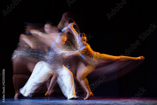 Energy in movements. Two professional dancers dancing ballroom dance isolated on dark background with mixed light. Concept of art, beauty, fashion