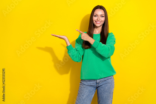 Portrait photo of young attractive confident smiling woman pointing holding hand empty space new ad isolated on yellow color background