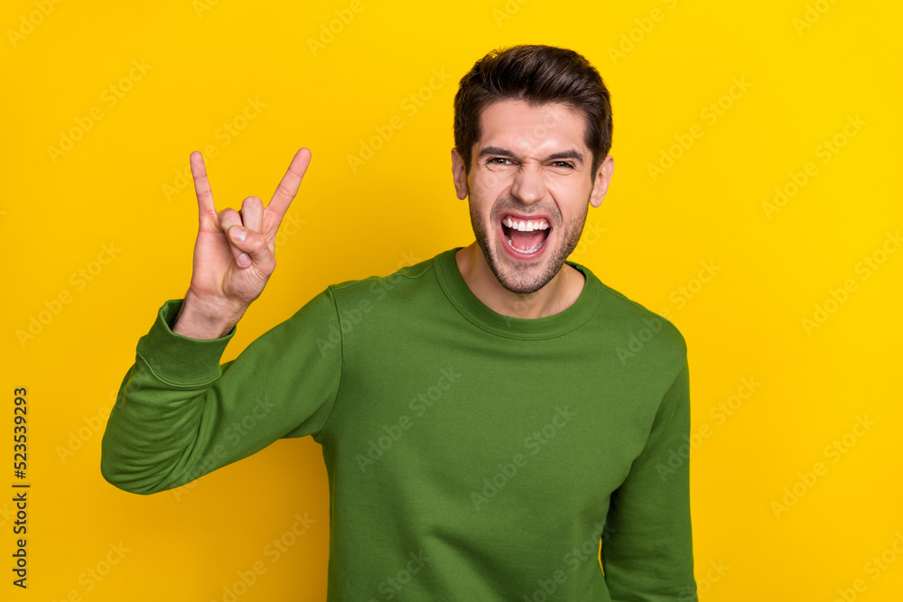 Photo of cool funny guy wear green sweater showing hard rock sign isolated yellow color background Photo of cool funny guy wear green sweater showing hard rock sign isolated yellow color background
