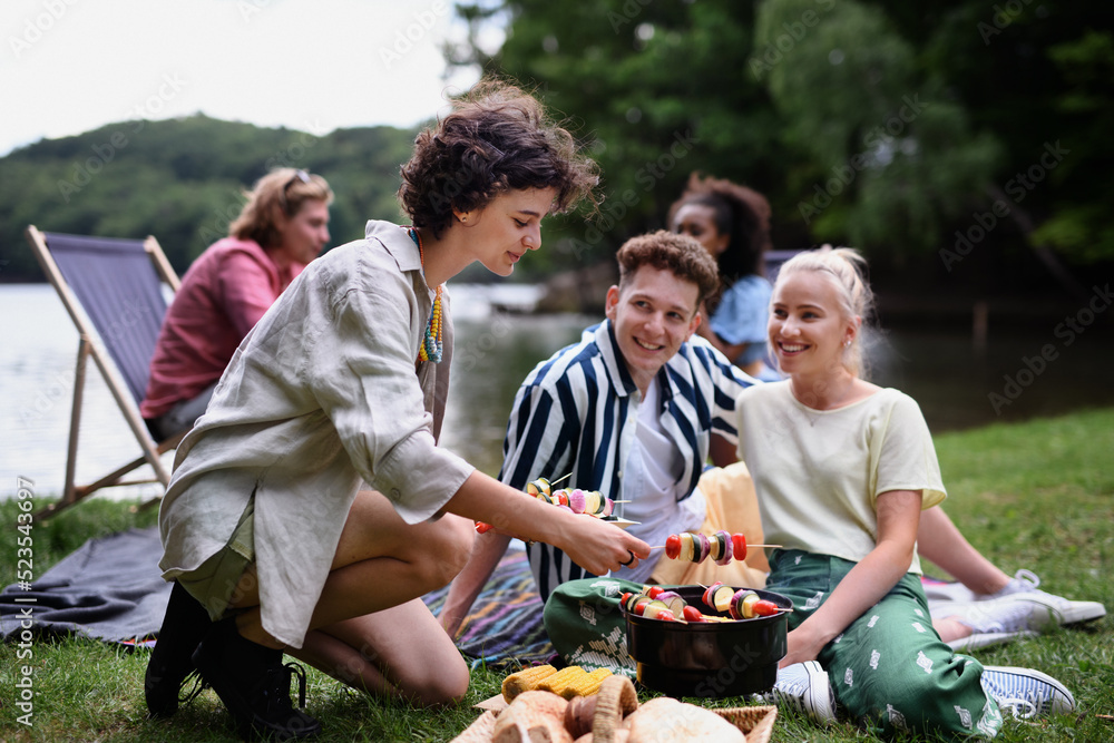 Fototapeta premium Group of multiracial young friends camping near lake and and having barbecue together.