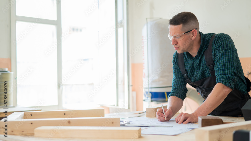 A portrait of a carpenter in goggles and work overalls draws a blueprint for a workshop. A portrait of a carpenter in goggles and work overalls draws a blueprint for a workshop.