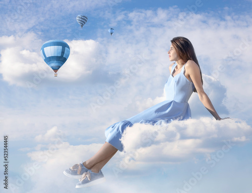 The girl is sitting on a cloud against the background of a blue sky with clouds. Balloons are flying in the background
