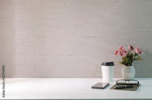 Comfortable workplace with paper cup  flower pot  smart phone and notebook on white table. Copy space for your advertise text.