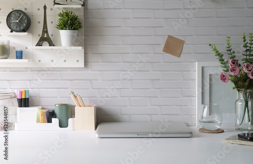 Creative workplace with laptop, picture frame, flower pot and stationery on white table. © wattana