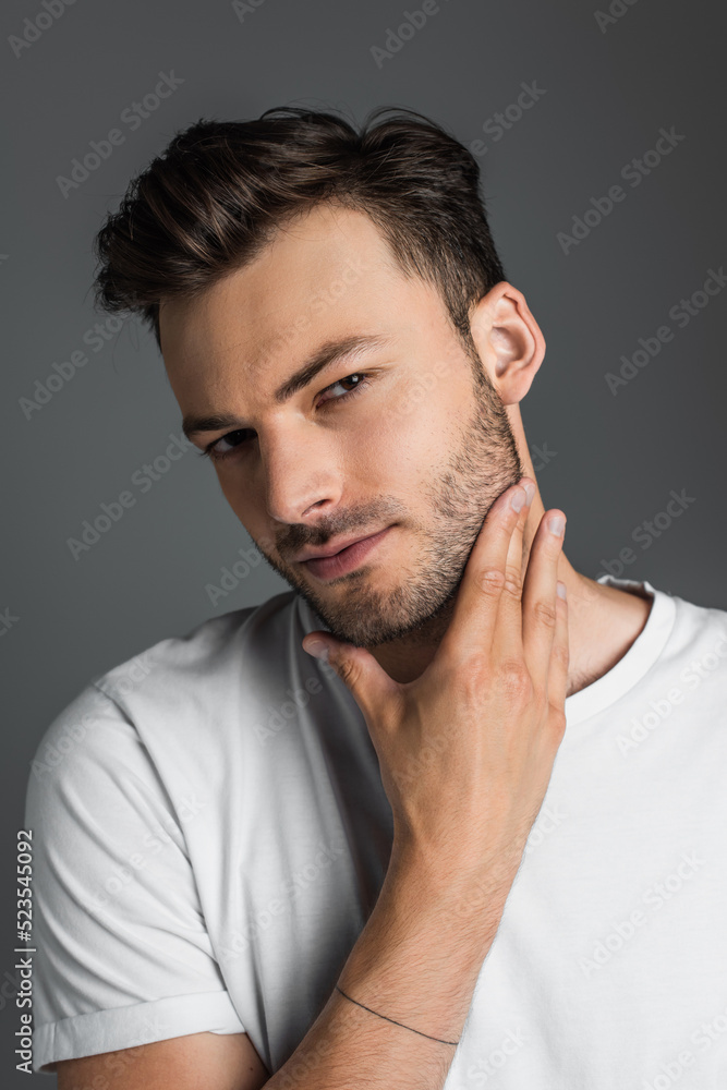 Portrait of brunette man touching beard and looking at camera isolated on grey. Portrait of brunette man touching beard and looking at camera isolated on grey.