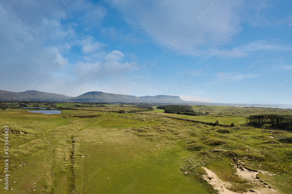 Green country side and Benbulben flat top mountain in county Sligo, Ireland. Warm sunny day. Aerial view. Irish landscape. Blue cloudy sky. Nature scenery.