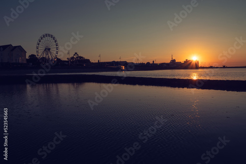Silhouette of Salthill promenade in Galway city at sunrise. Warm orange color. Calm peaceful mood. Fun wheel on the left. © mark_gusev