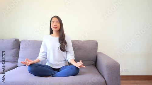 Dressed in jeans and a sweater, a young woman with closed eyes strikes a yoga pose on a couch. Title space photo