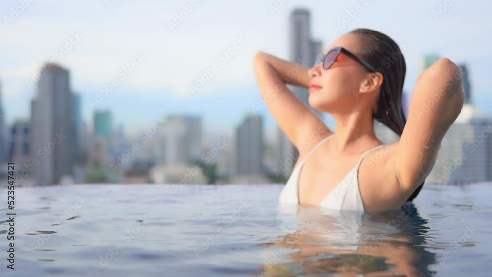 A beautiful woman in a rooftop swimming pool smooths back her wet hair. There is a modern urban skyline in the background. A beautiful woman in a rooftop swimming pool smooths back her wet hair. There is a modern urban skyline in the background.
