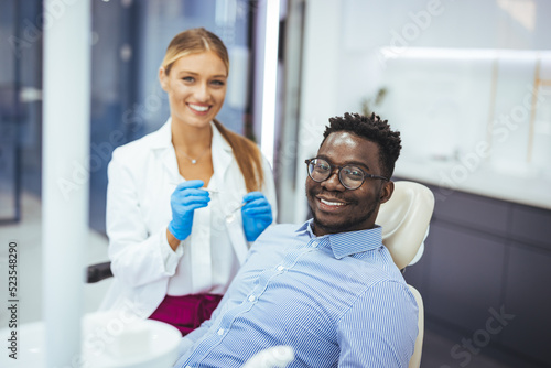 Smiling african guy in dentist chair looking with trust at his doctor  close up. Young African American Man Getting Teeth Treatment With Professional Stomatologist At Modern Clinic